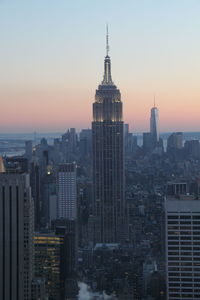 Empire state building in city against sky during sunset