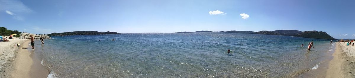 Panoramic view of people on beach against blue sky