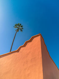 Low angle view of building and palm tree against blue sky