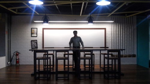 Rear view of man standing in illuminated room