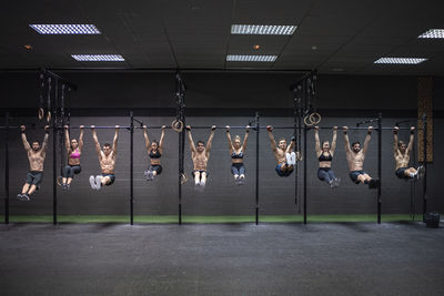 Male and female athletes hanging on rod at gym