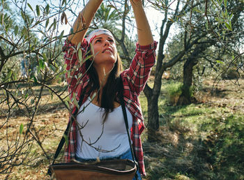 Young woman looking away while standing on tree in forest