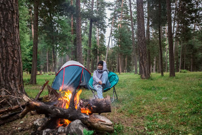 Woman sitting by campfire in forest