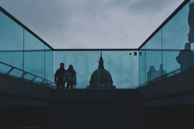 Rear view of people standing by railing against sky
