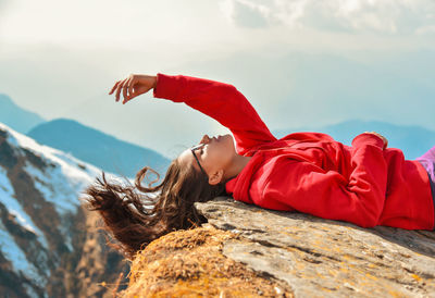 Woman lying on rock against sky