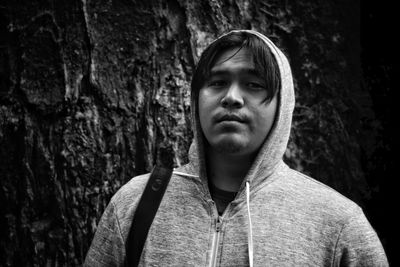 Portrait of young man standing against tree trunk