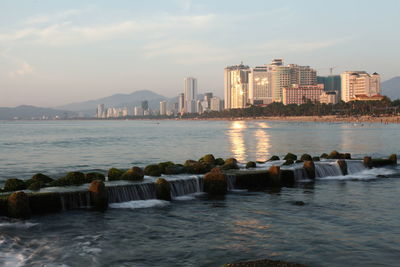 Sea by buildings against sky in city