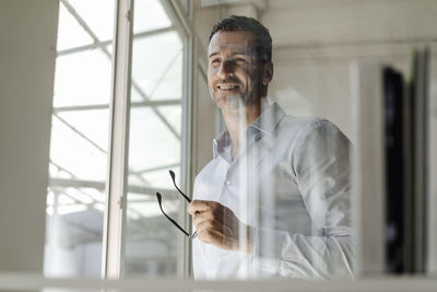 Smiling businessman holding glasses standing at the window