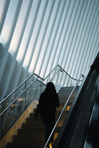 Rear view of silhouette man walking on escalator in building