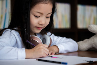 Close-up of girl writing on book at desk