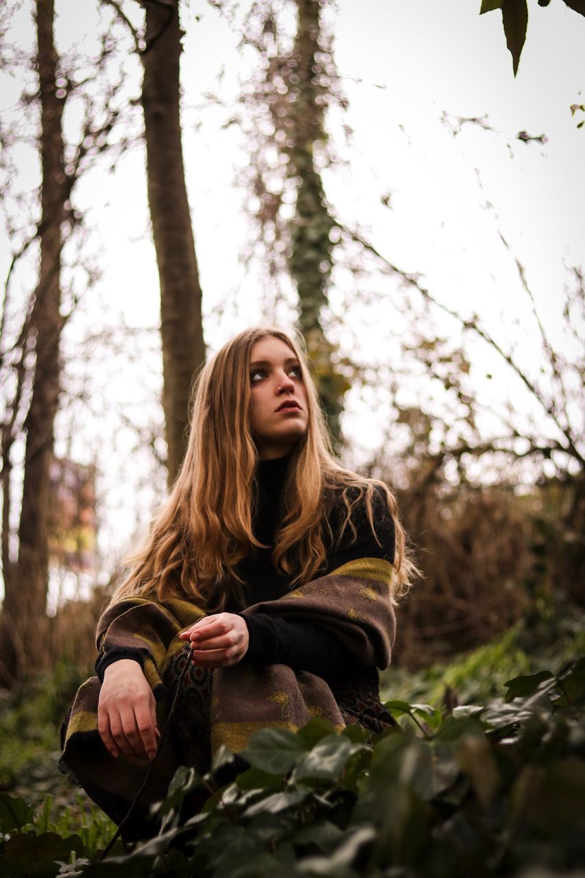 tree, plant, one person, long hair, forest, young adult, land, nature, hair, real people, young women, hairstyle, lifestyles, leisure activity, front view, beautiful woman, beauty, day, sitting, outdoors, contemplation, woodland