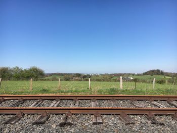 Railroad track amidst field against clear blue sky