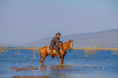 Man riding horse in lake against clear sky