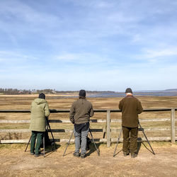 Rear view of people standing on field against sky