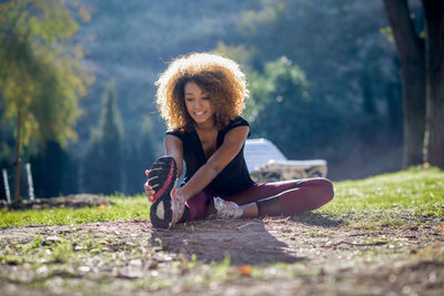 Full length of young woman exercising on field during sunny day