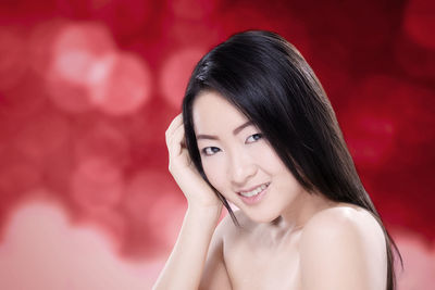 Portrait of shirtless young woman against red background
