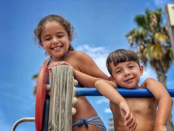 Portrait of happy siblings against blue sky