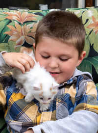 Young boy plays with an active white kitten as it crawls all over him