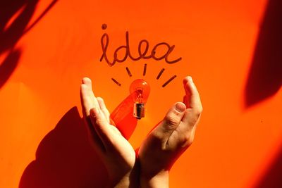 Cropped hands with light bulb and idea text on orange table