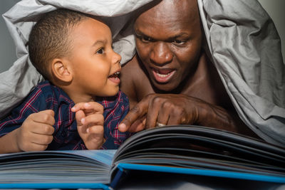 Father reading a book for his son under the blanket