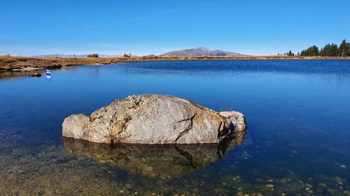 Rock formation in lake against blue sky