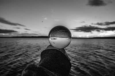 Close-up of person holding sunglasses against sea during sunset