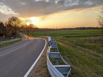 Road amidst field against sky during sunset