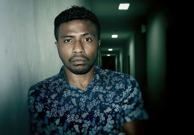 Portrait of young man standing in illuminated corridor