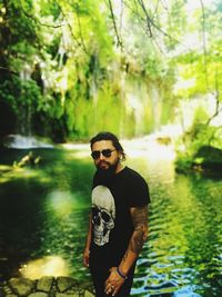 Portrait of man wearing sunglasses standing against lake in forest