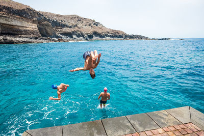 Full length of shirtless man jumping in sea against sky