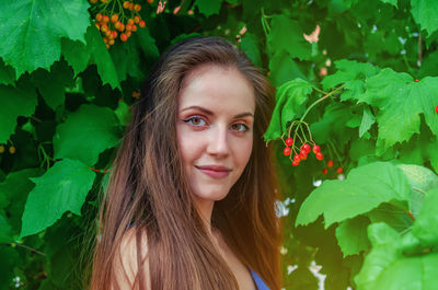Attractive woman with long hair looks into the camera with half turn on background of viburnum bush