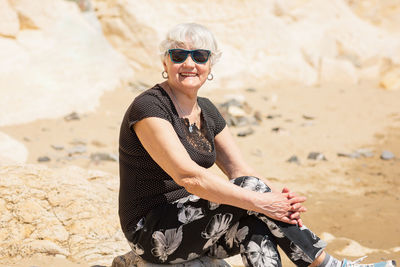 Old woman in black clothes sitting on a rock near the sea