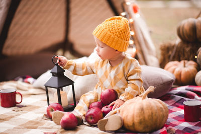 Cute baby girl 1-2 year old holding red tasty apples, pumpkin and candle outdoors. autumn season.