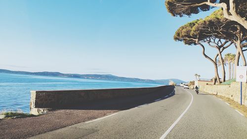 Road by sea against clear blue sky