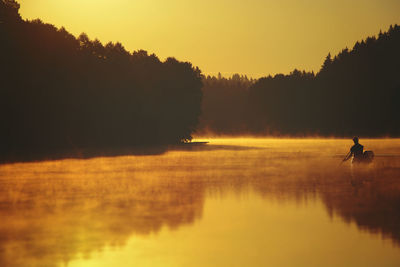 Silhouette of man by lake against sky during sunset