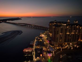 High angle view of illuminated city by sea against sky at sunset