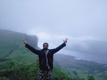 Smiling man with arms raised standing against mountain