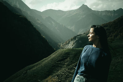 Side view of woman standing against mountains and sky
