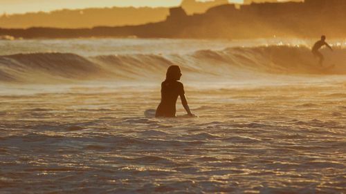 Silhouette boy on shore against sea during sunset