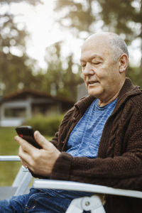 Senior gay man using smart phone sitting at yard