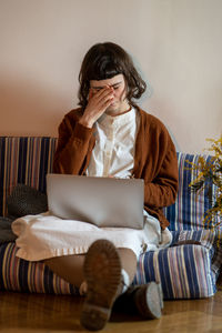 Tired teenage hipster girl working, studying with laptop from home, closing eyes of fatigue