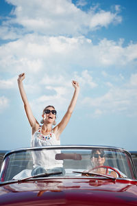 Low angle view of woman with arms raised against sky