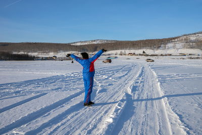 A woman holding up her hands in a winter lake against shore and fishermen.