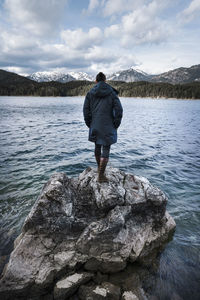 Rear view of man standing on rock by lake against sky