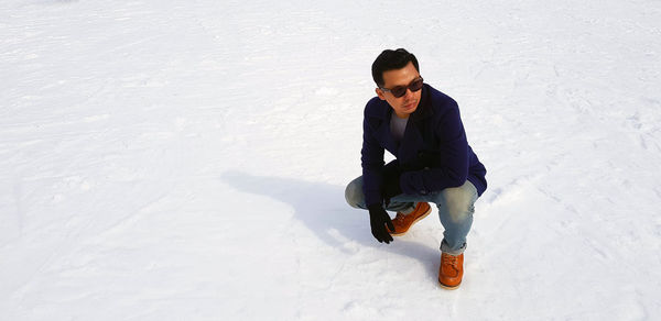 High angle view of young man sitting in snow