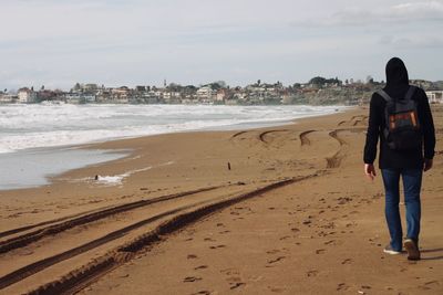 Rear view of man walking on beach against sky