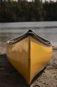 Close-up of a yellow canoe on a sandy beach by a lake.