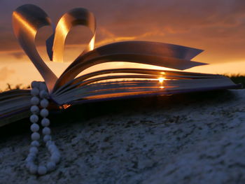 Bead necklace with heart shape folded pages of book during sunset