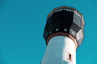 Low angle view of watertower against building against clear blue sky