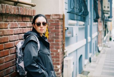 Woman wearing sunglasses standing against brick wall